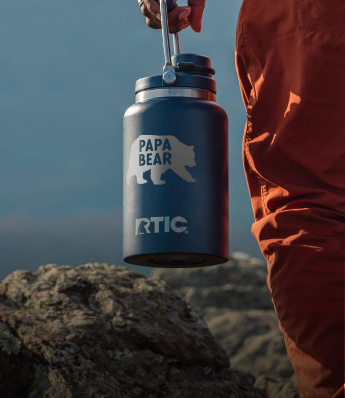 Person walking outside, carrying a navy blue RTIC Outback Jug.