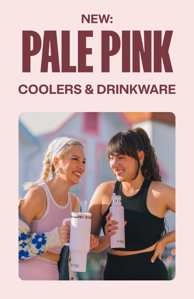 Two women in athletic wear laugh together outdoors, holding pink RTIC drinkware in front of a pastel house on a sunny day.