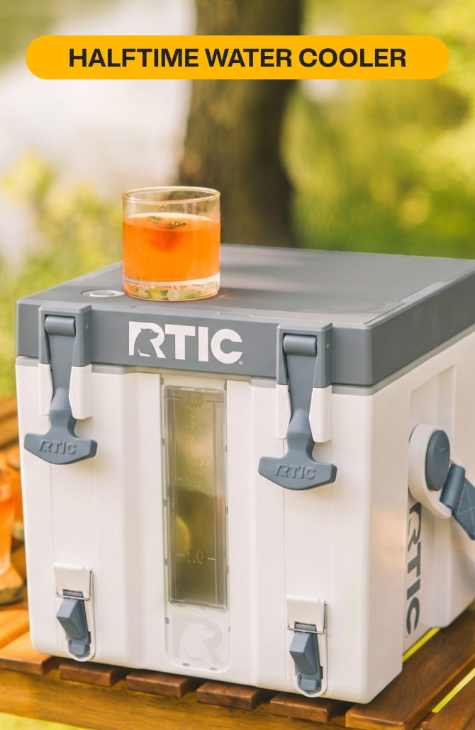 White RTIC Halftime Water Cooler sitting on a table with an orange cocktail.