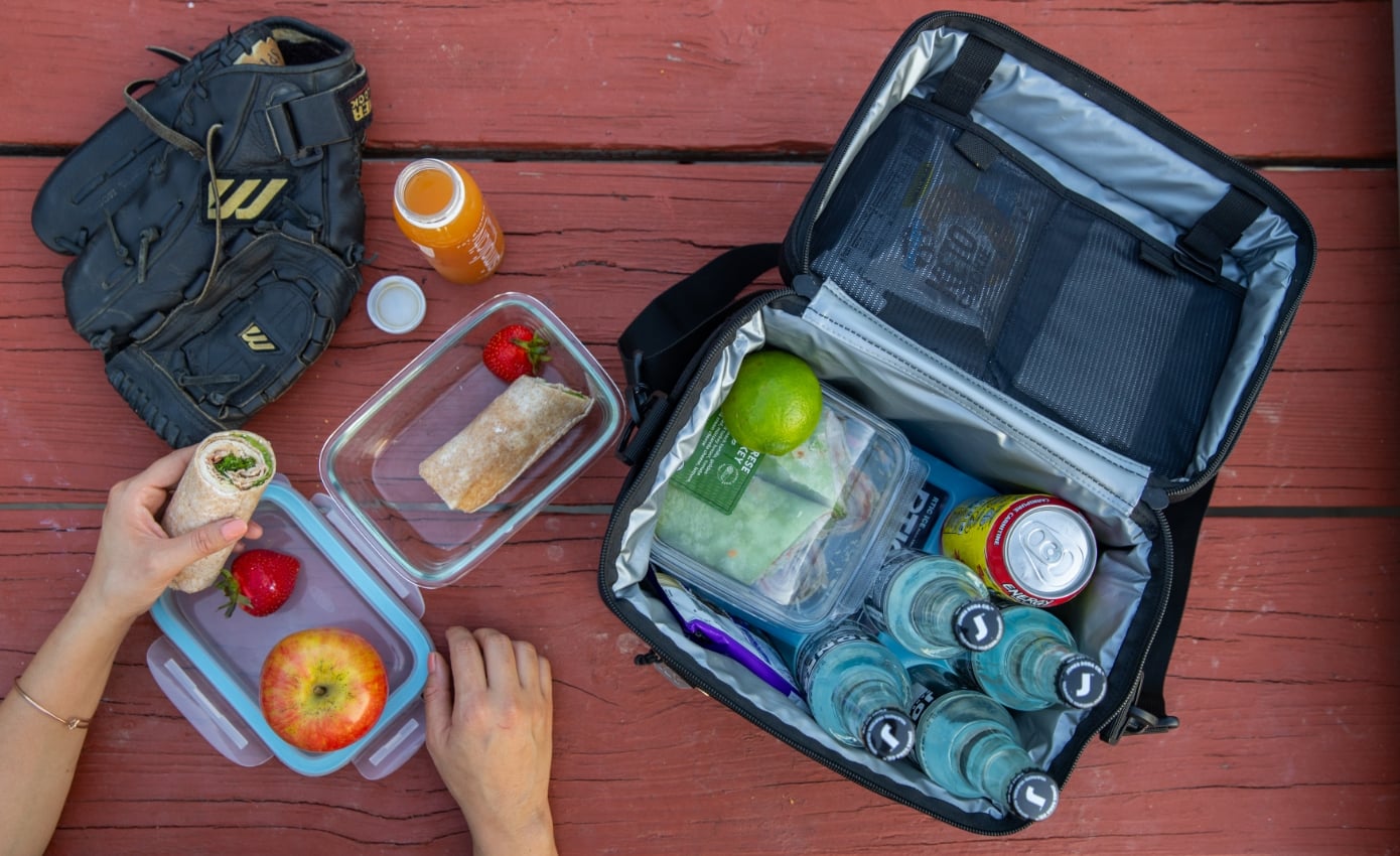 A person getting a drink out of a green RTIC waterproof soft cooler filled with ice.