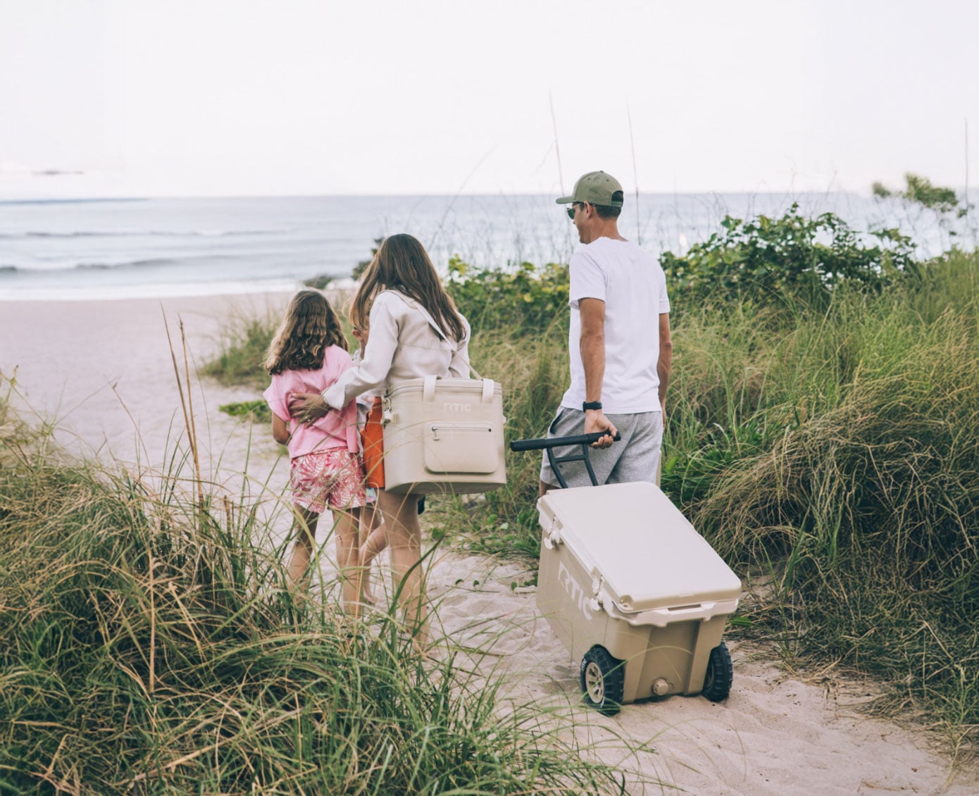A family pulling an RTIC wheeled cooler and carrying an RTIC soft cooler to the beach.