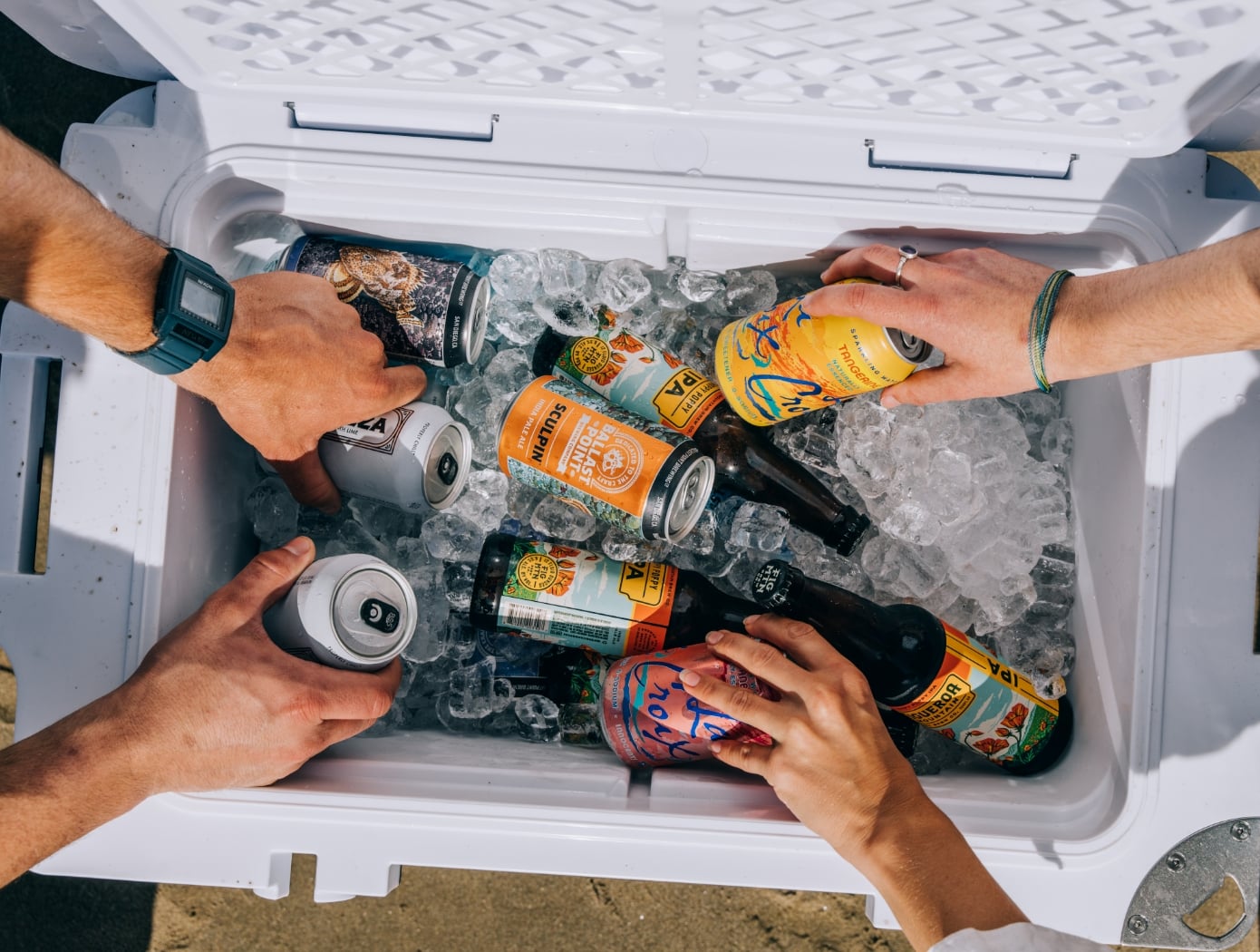People reaching into a RTIC hard cooler full of ice and drinks.
