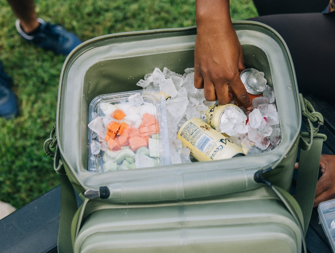 A person getting a drink out of a green RTIC waterproof soft cooler filled with ice.