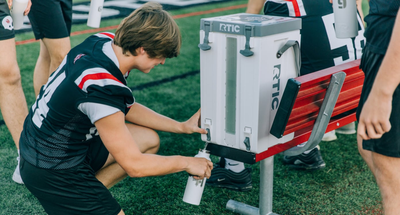 A football player getting water from a white RTIC Halftime Cooler.