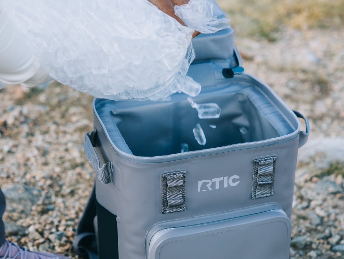 Ice being poured into a grey RTIC waterproof backpack cooler.