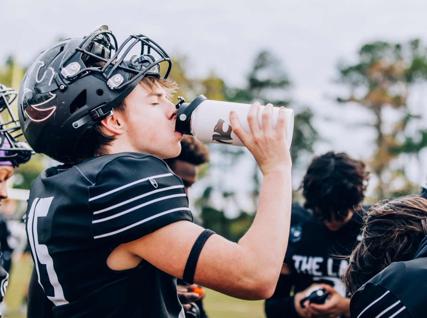 A football player drinking from a white RTIC Outback Bottle.