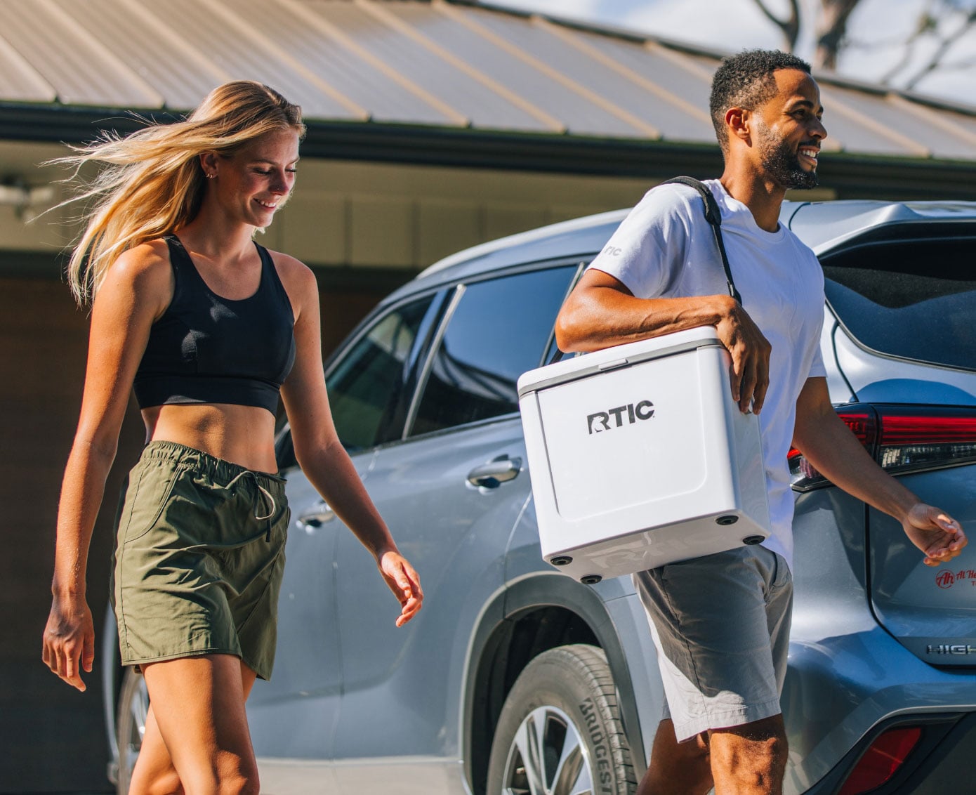 Two people walking to the car with a a white RTIC Road Trip Cooler.