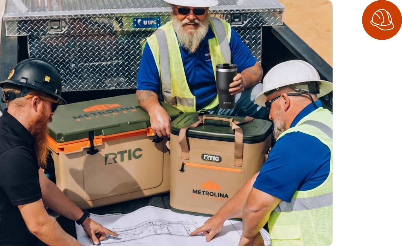 A trio of professionals in hard hats studying construction drawings next to customized RTIC coolers.