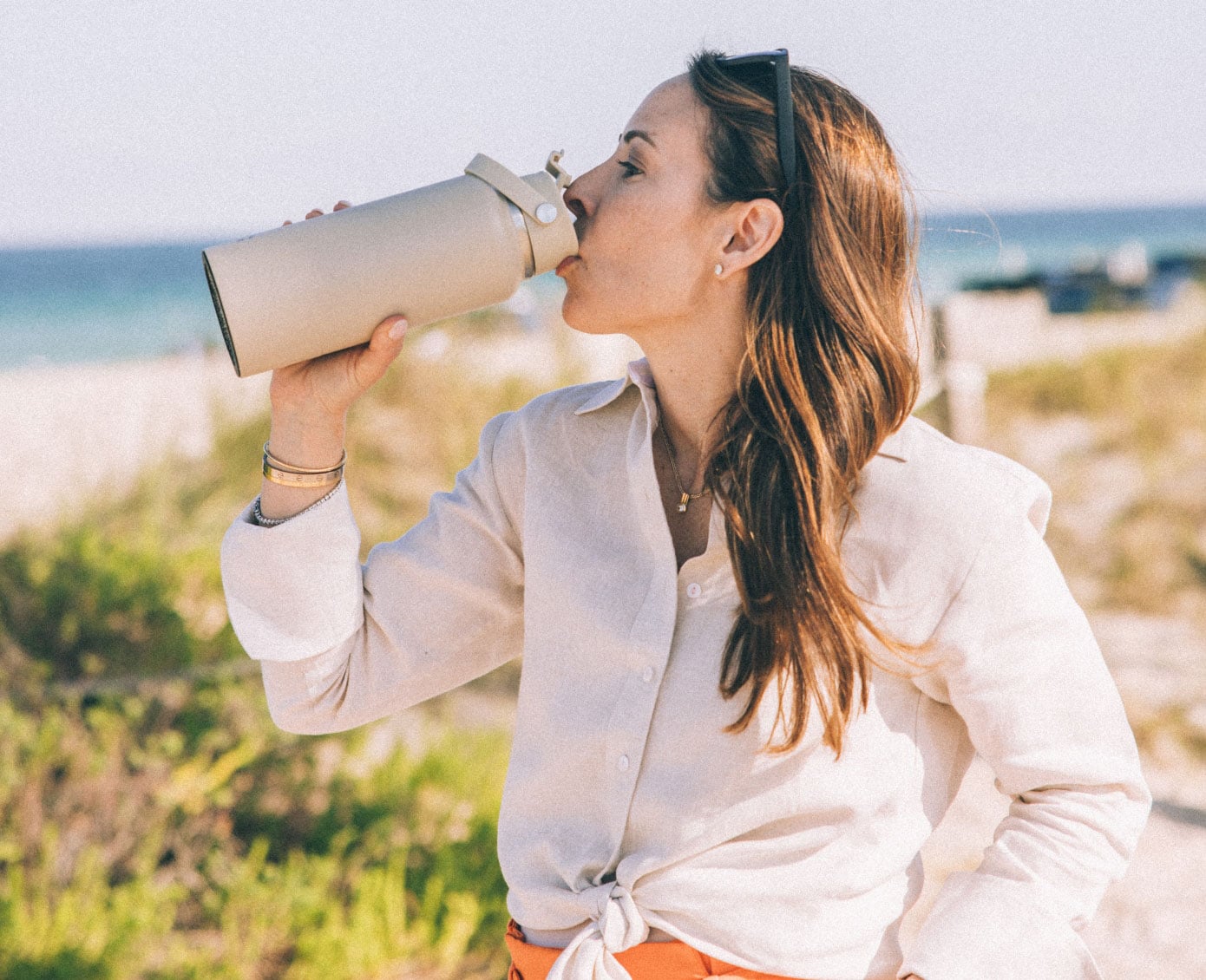 A woman at the beach, drinking from a tan RTIC Bottle.